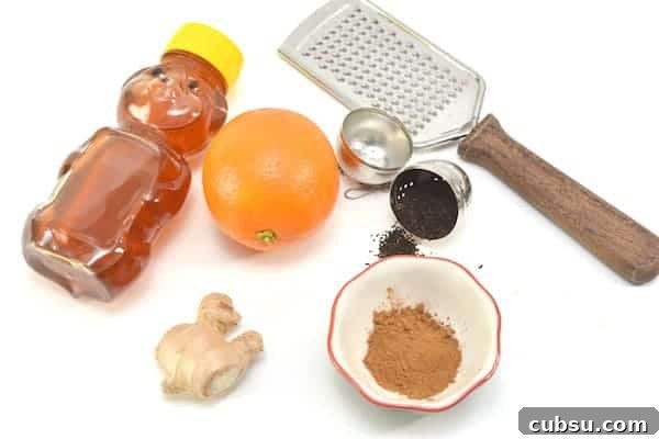 Citrus Spice Detox Tea Recipe for Gut Cleansing and Energy 4 Image shows the ingredients for orange detox tea spread out on a white counter. It includes a bottle of honey, an orange, ginger root, a small dish of cinnamon, black tea, and a grater to grate the ginger.