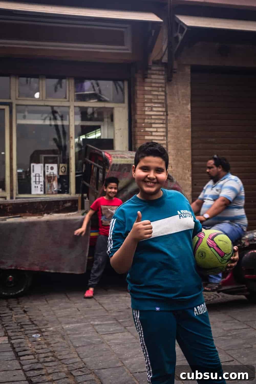 Cairo Adventures: Top Experiences and Hidden Gems to Explore 10 portrait shot of a kid holding soccer ball, posing with at thumbs up in Old Cairo.