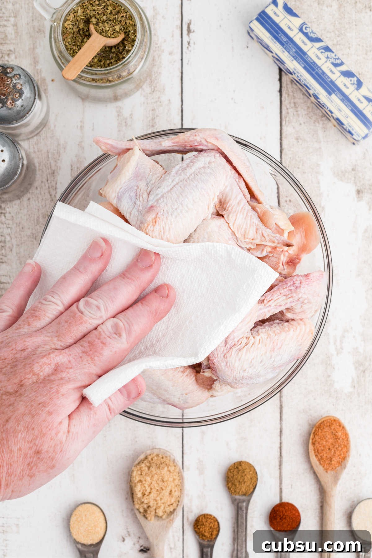 A bowl of chicken wings being patted dry with a paper towel.