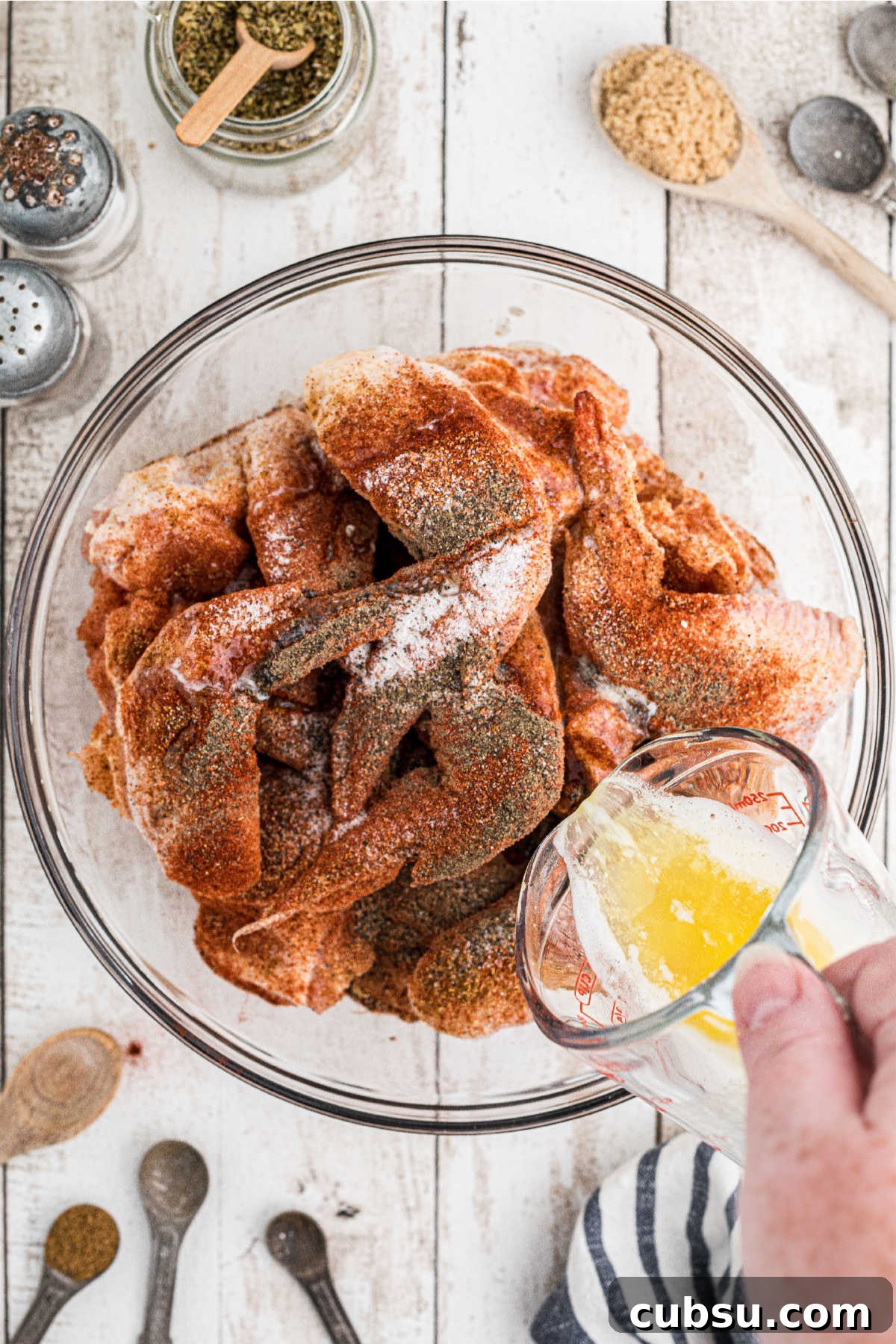 Butter being poured over seasoned chicken wings.