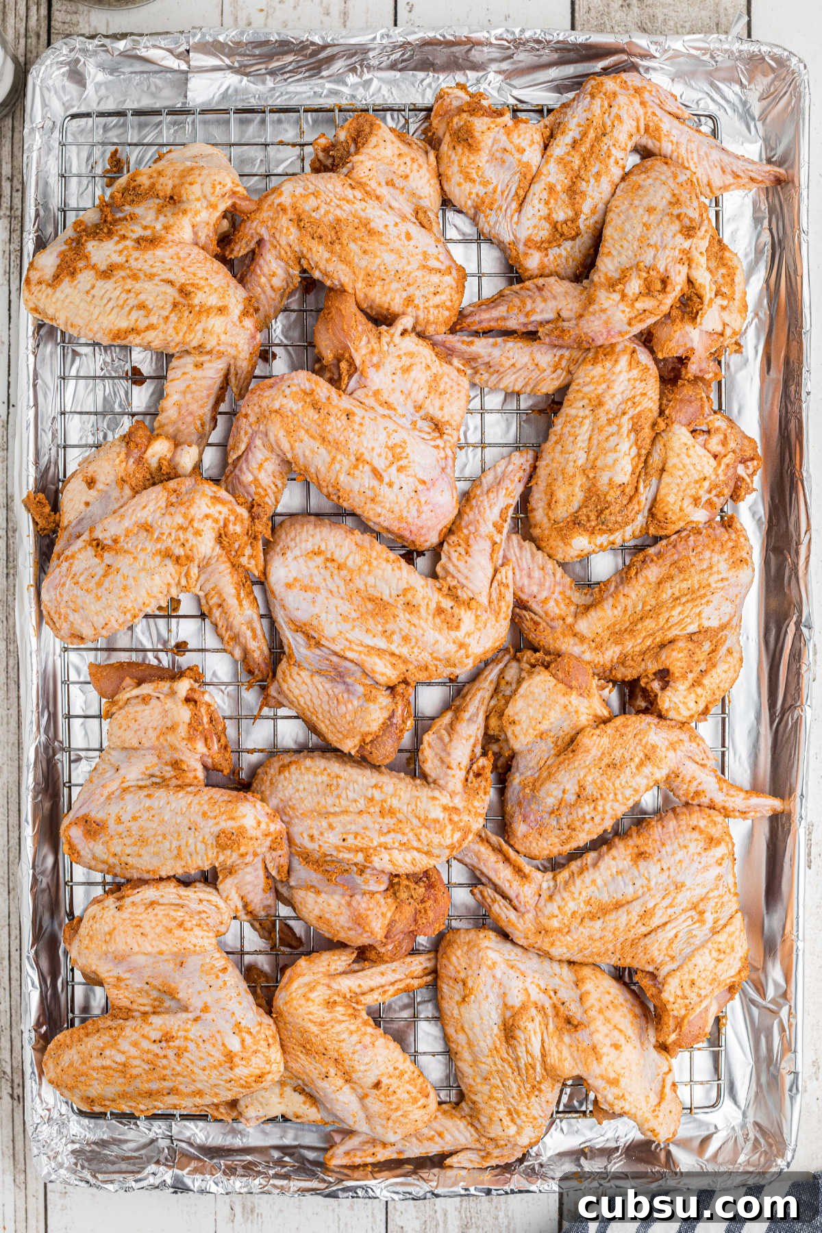 Seasoned chicken wings arranged on a baking sheet with a wire rack.