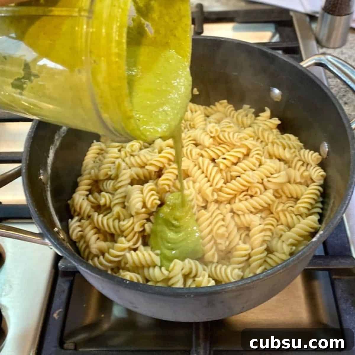 Vegan Pesto Pasta Recipe I am adding pesto sauce to the cooked noodles in a pan.