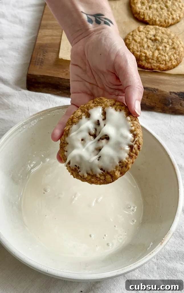 Zesty Lemon Oatmeal Cookies with a Refreshing Iced Glaze 7 Hand holding an iced cookie over a bowl of vanilla icing.