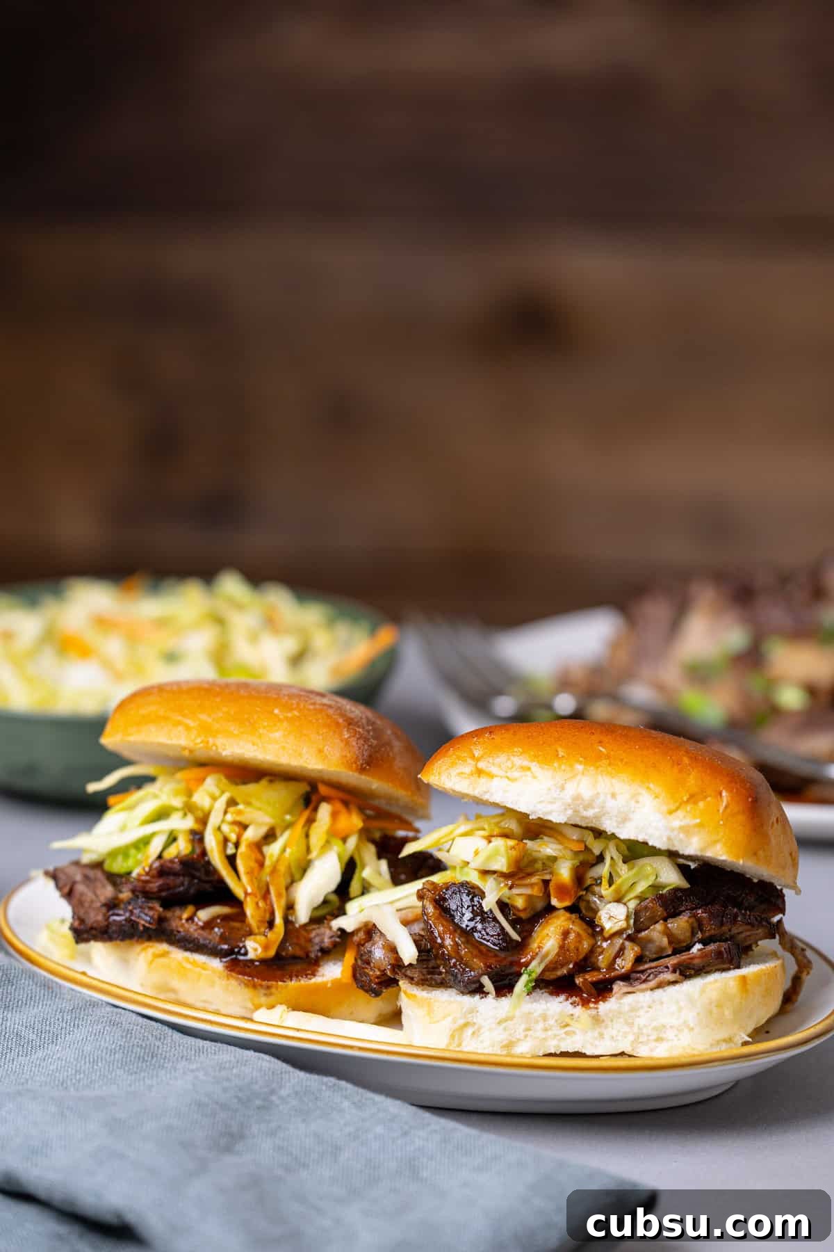 Citrus Slaw Braised Beef Sliders – Tangy Gourmet Sandwiches 2 A close up of two braised beef sliders topped with citrus slaw.