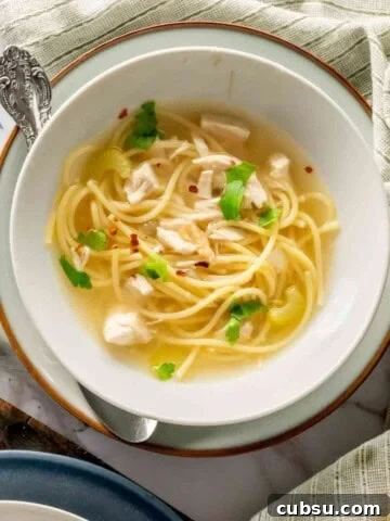 Chicken noodle soup with breadsticks and gray linen napkins.