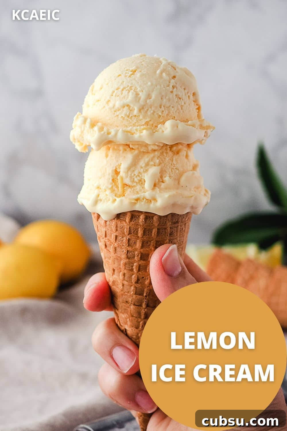 Creamy Lemon Ice Cream Recipe: Bright, Tangy Homemade Treat 11 Hand holding two scoops of ice cream in a cone with lemons in the background and text overlay, lemon ice cream.