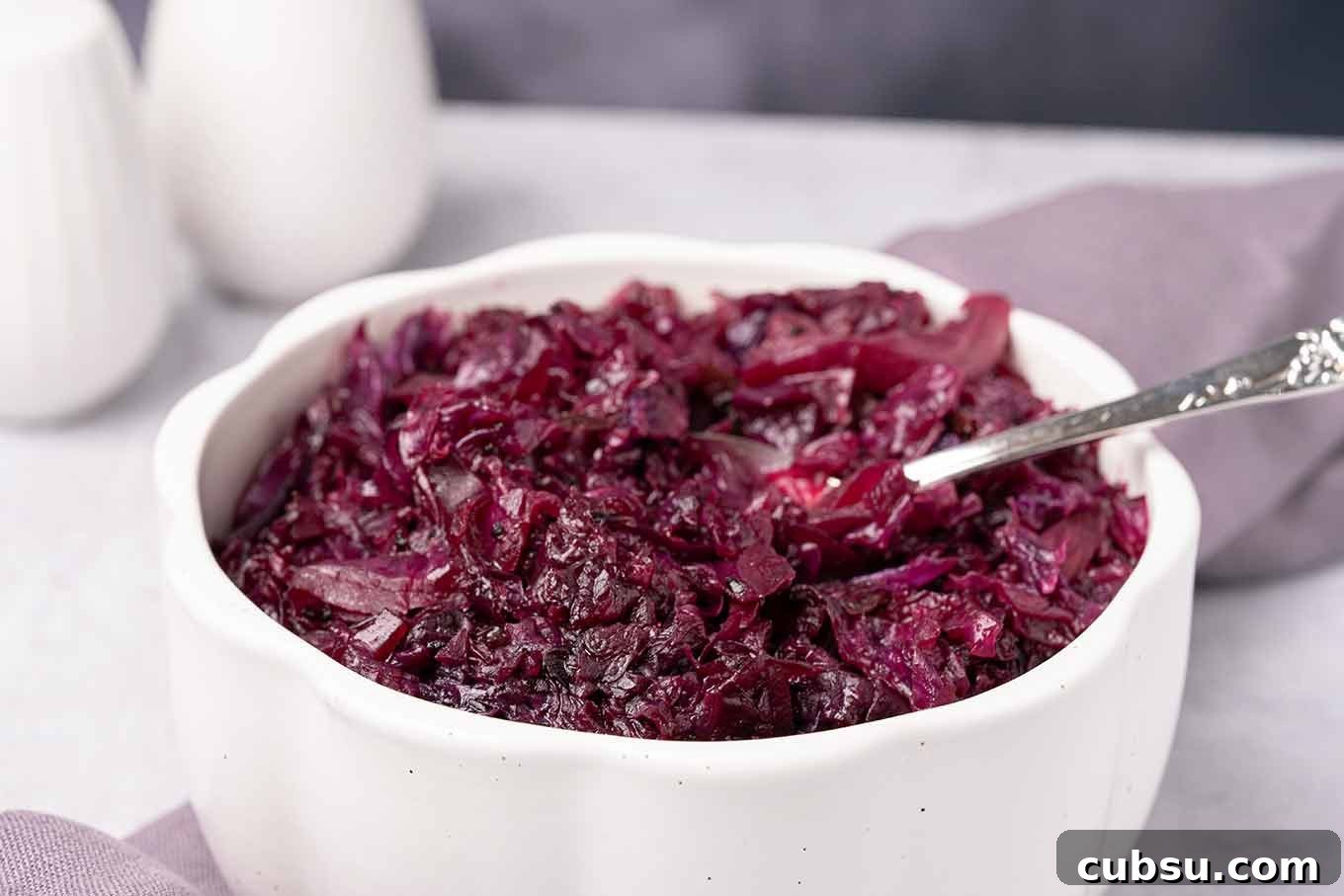 Slow-Braised Red Cabbage with Apple and Balsamic Glaze 3 A serving bowl of red cabbage that was braised in apple cider and currant jelly with a serving spoon in it.