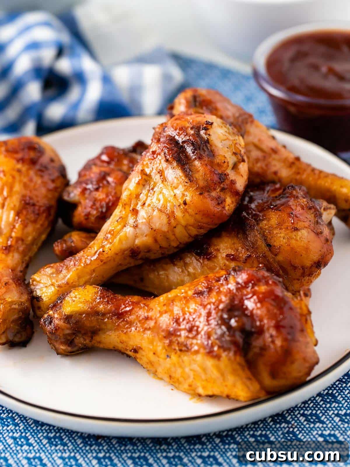  A plate of smoked chicken legs on the table with a blue and white checkered napkin.