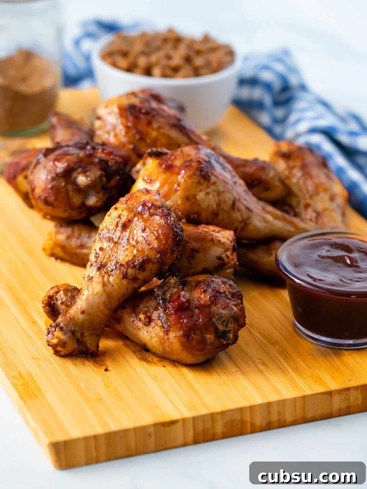 Chicken legs in the smoker on a cutting board with a ramekin of bbq sauce in the back.