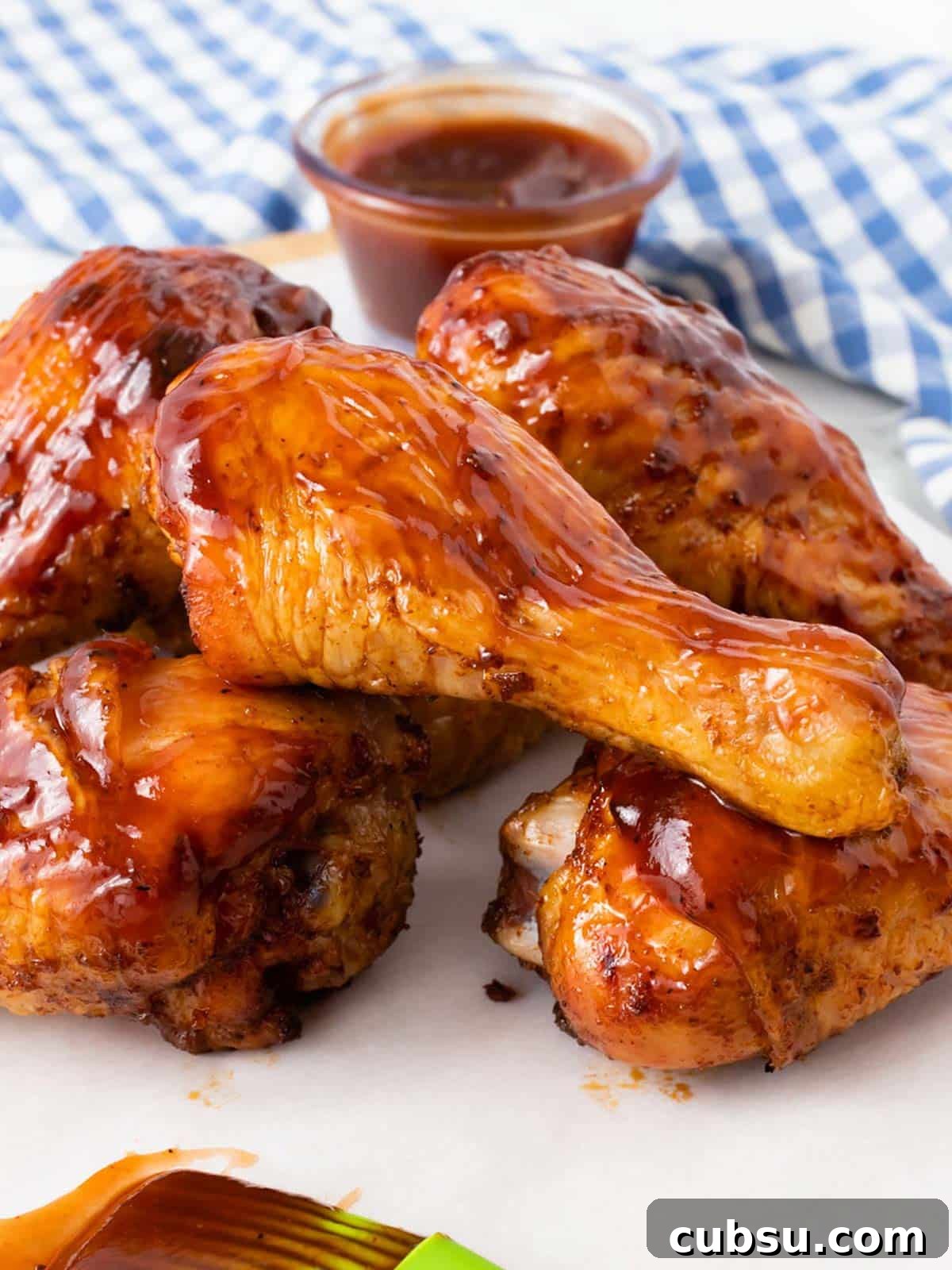 A stack of smoked chicken legs on a plate with bbq sauce.