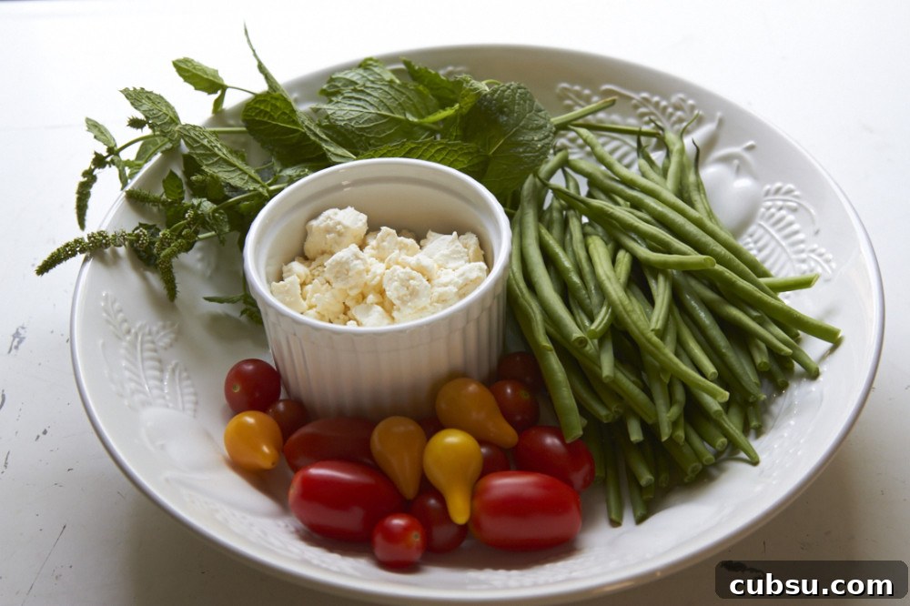 Mediterranean Green Bean Salad with Tomatoes, Feta & Mint 3 Fresh mint, green beans, tomatoes, and feta cheese in a large white bowl.