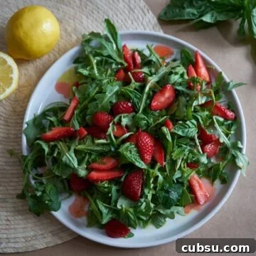 A plate of salad with arugula, herbs, and sliced strawberries.