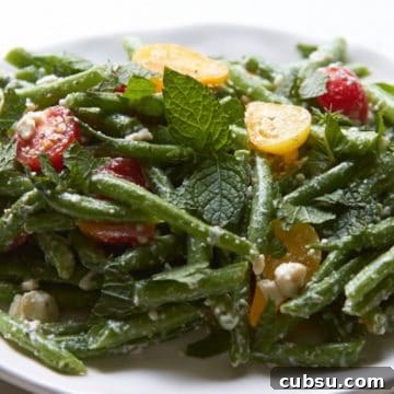 Mediterranean Green Bean Salad with Tomatoes, Feta & Mint 9 Green bean salad with feta and mint on a white plate.