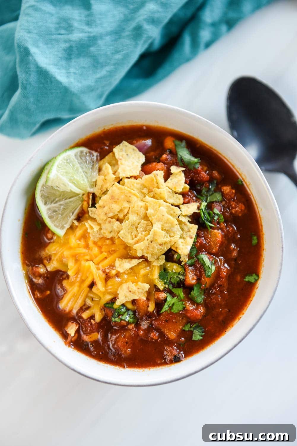 overhead view of bowl of turkey chili topped with sliced limes, shredded cheese and tortilla chips