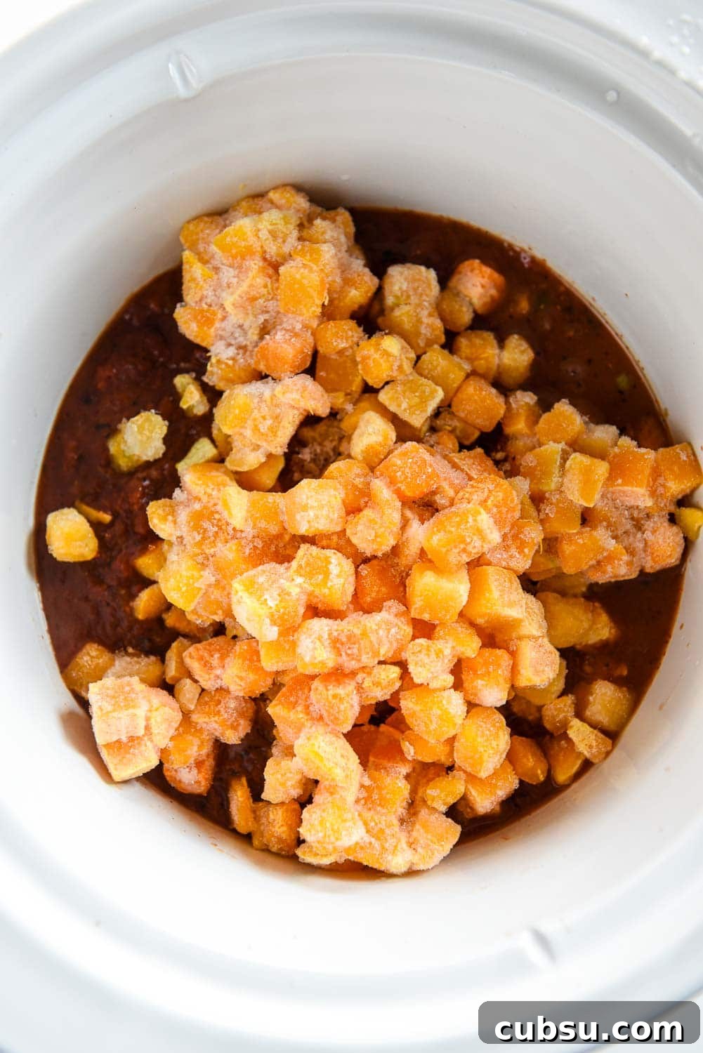 slow cooker with chili ingredients topped with frozen butternut squash