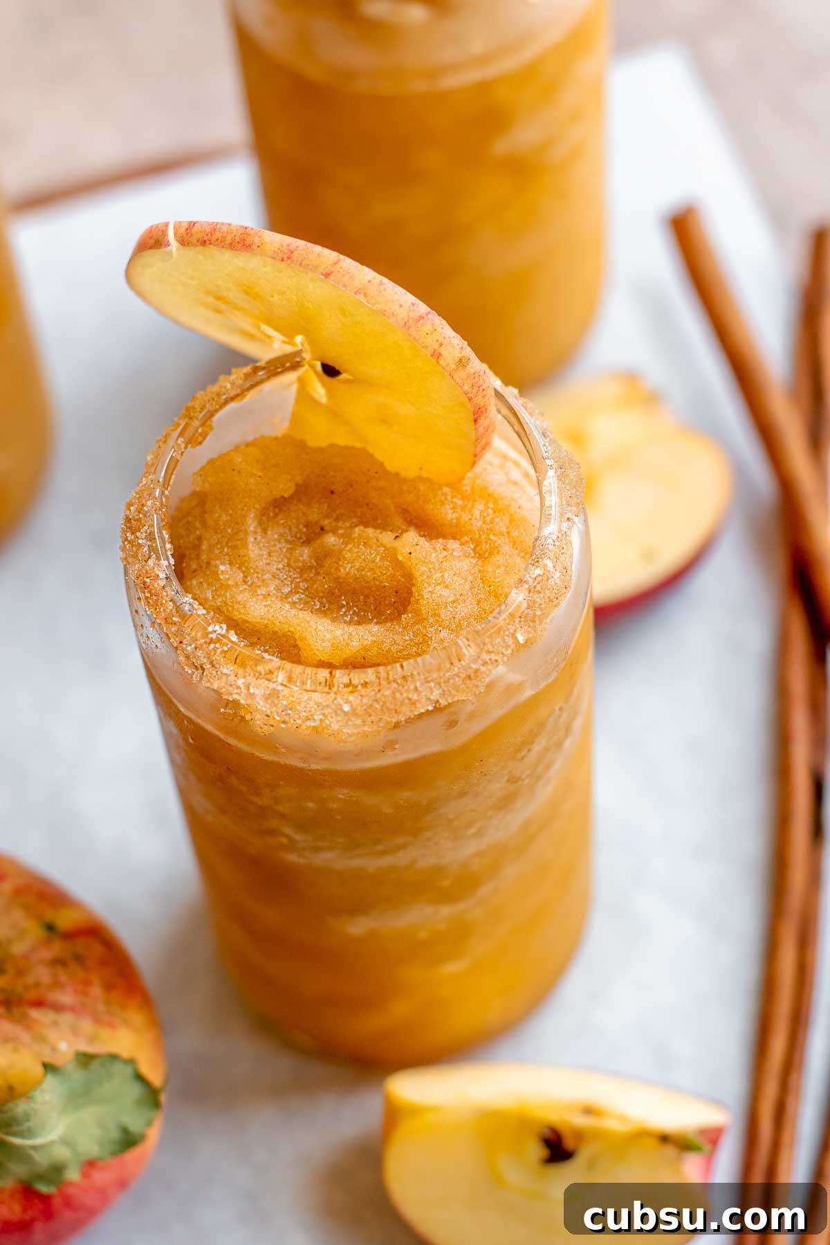 Spiced Apple Cider Slushies — Boozy or Virgin Recipes for Fall 12 Apple cider slushie in a glass with a slice of apple in the top.