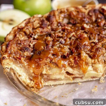 Caramel apple pie in a a pie dish with caramel drizzling over a cut slice.
