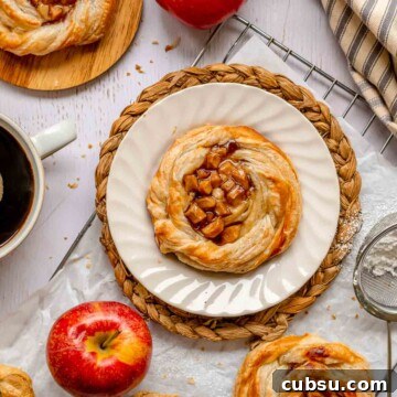 Apple danish on plate with apples and coffee around the plate.