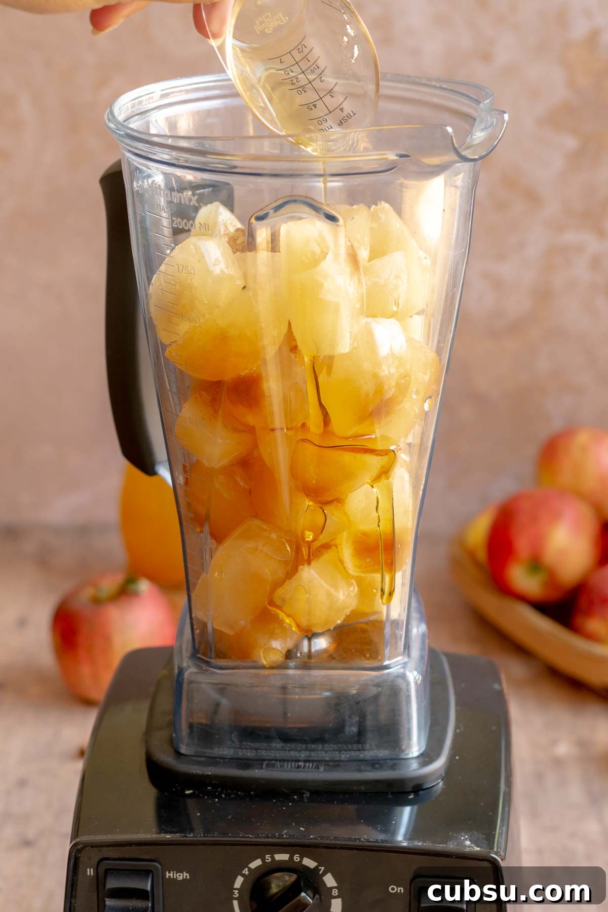 Spiced Apple Cider Slushies — Boozy or Virgin Recipes for Fall 8 A hand pours maple syrup into a blender full of apple cider ice cubes.