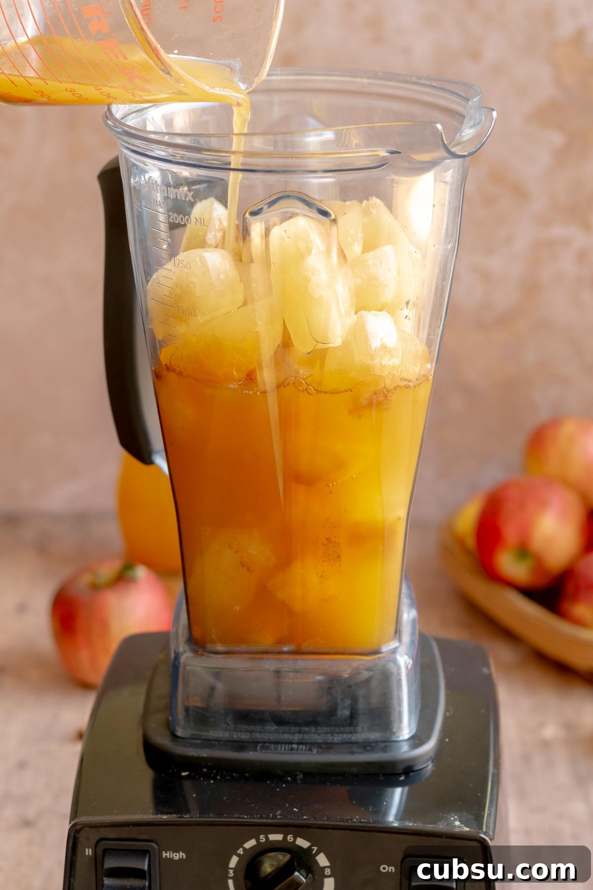 Spiced Apple Cider Slushies — Boozy or Virgin Recipes for Fall 9 A hand pours apple cider over apple cider ice cubes in a blender.