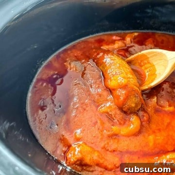 A crock pot filled with sausages, peppers and marinara sauce.
