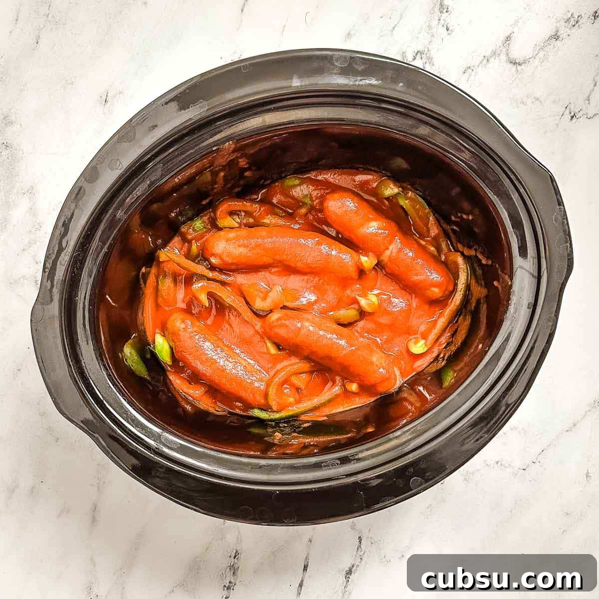 A crock pot filled with sausage, peppers and marinara sauce.