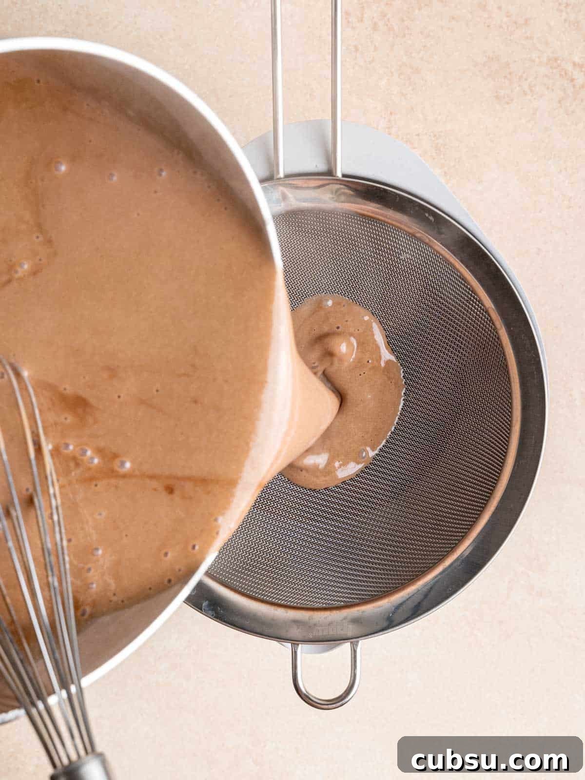 Pouring the malt chocolate ice cream mixture into a bowl through a fine mesh sieve.