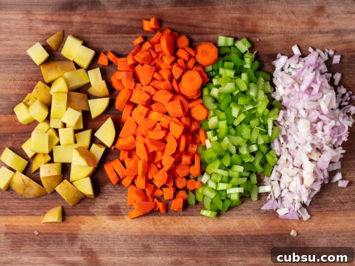 Chopped Yukon gold potato, carrots, celery, and shallots lined up on a cutting board