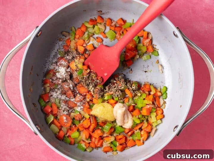 Sautéed vegetables in a pot with garlic, ginger, dried basil, red pepper flakes, salt, and pepper