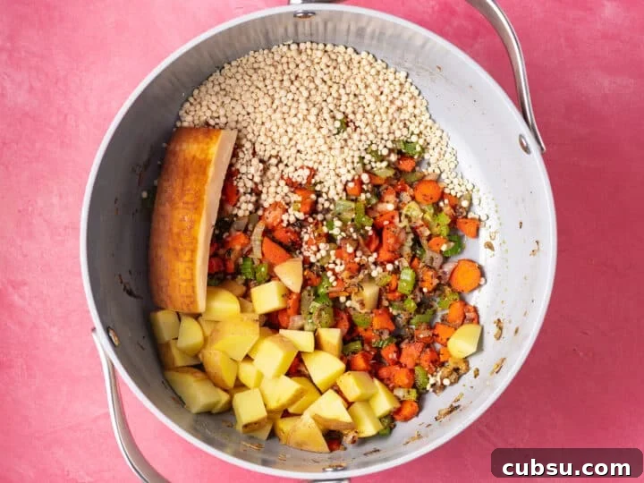 Pearl couscous, diced potatoes, and a parmesan rind added to sautéed vegetables in a soup pot