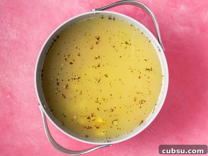 Vegetable broth in a pot with herbs and a parmesan rind before simmering
