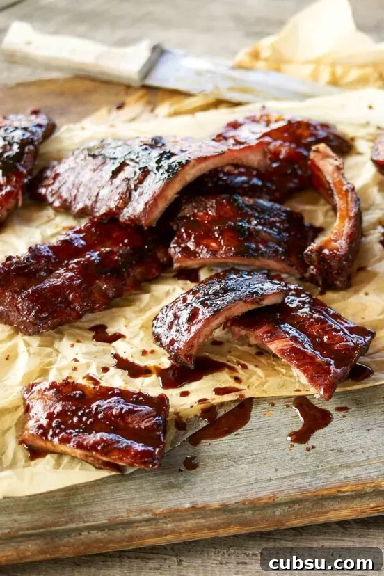 Sticky pork ribs cut into individual ribs on a piece of parchment with a knife.