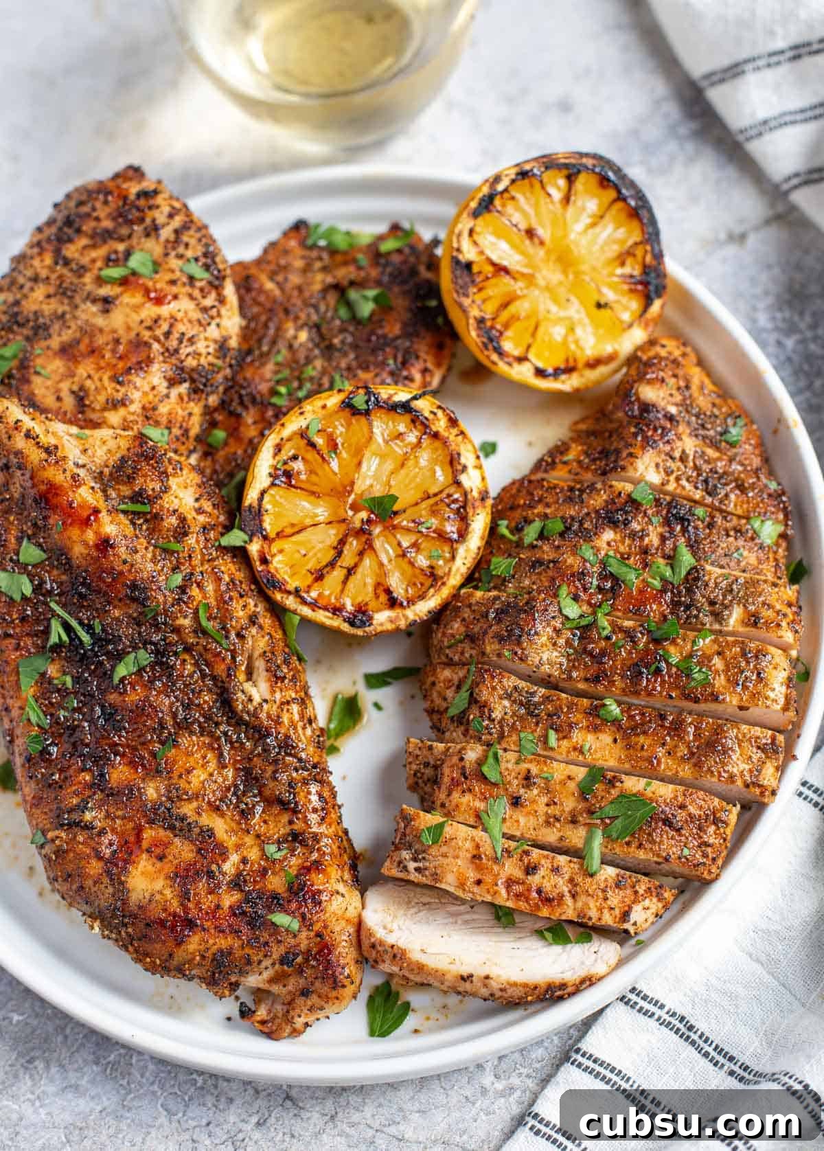 Grilled boneless skinless chicken on a plate with grilled lemon garnish.