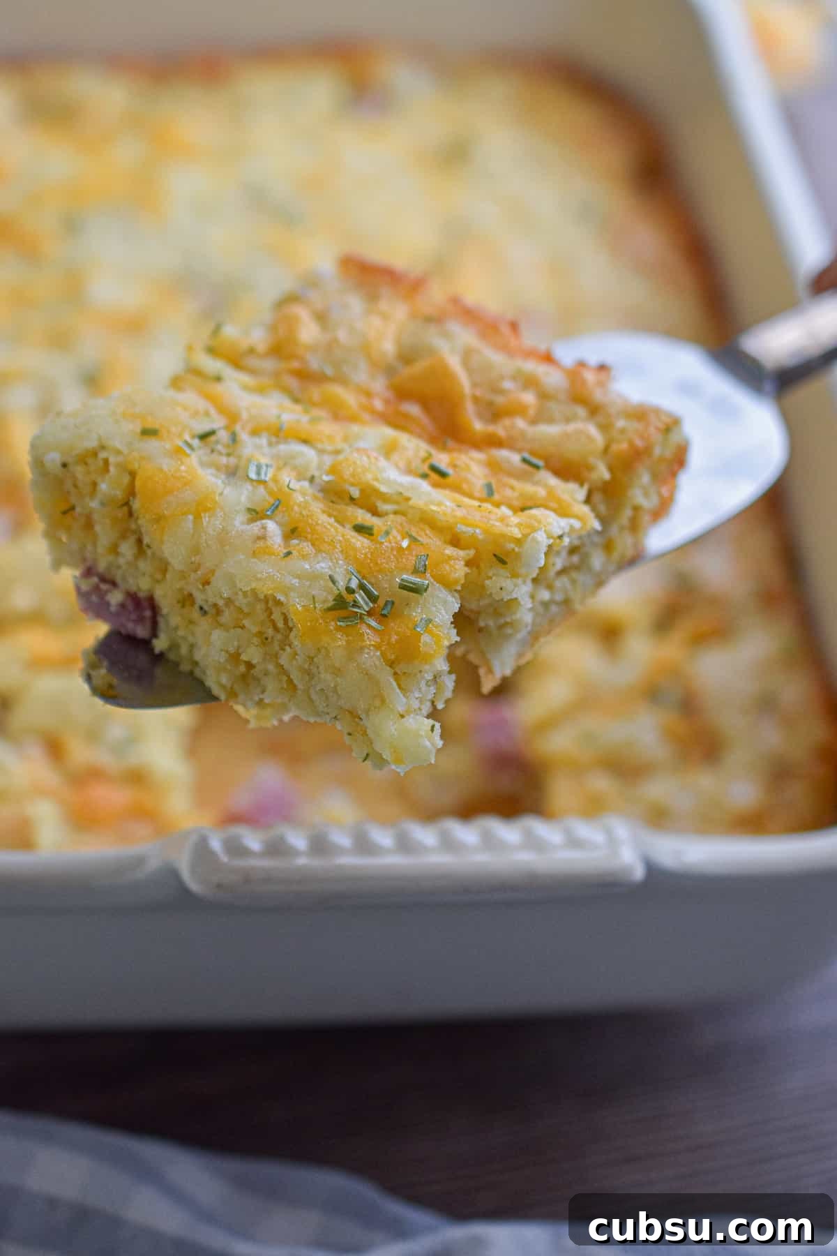 A pie cutter is holding a piece of the bisquick breakfast casserole over the casserole dish.
