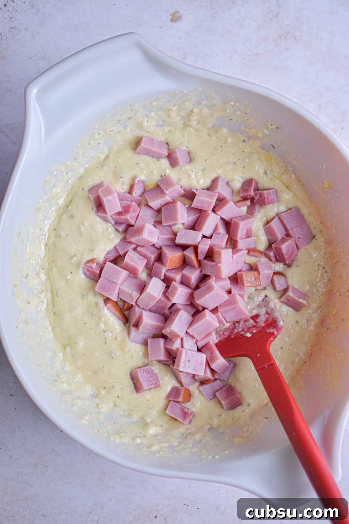 The ham is added to the large mixing bowl.