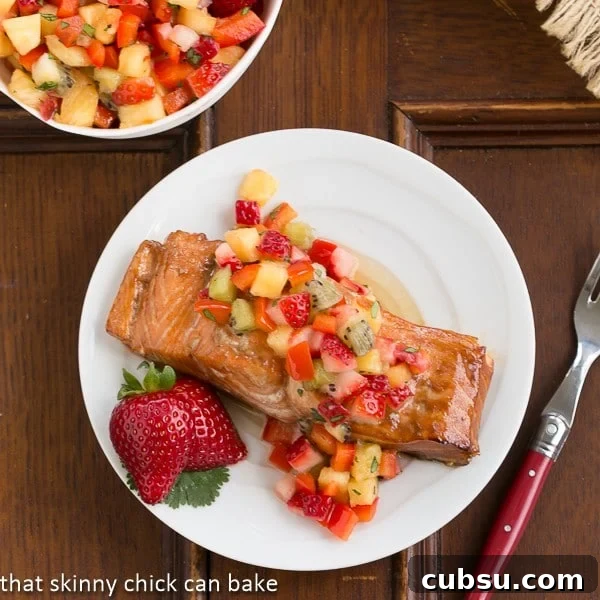 Strawberry Salsa Topped Salmon - Roasted Asian inspired salmon topped with fruit salsa Overhead view of Strawberry Salsa Topped Salmon on a white plate with a red handled fork