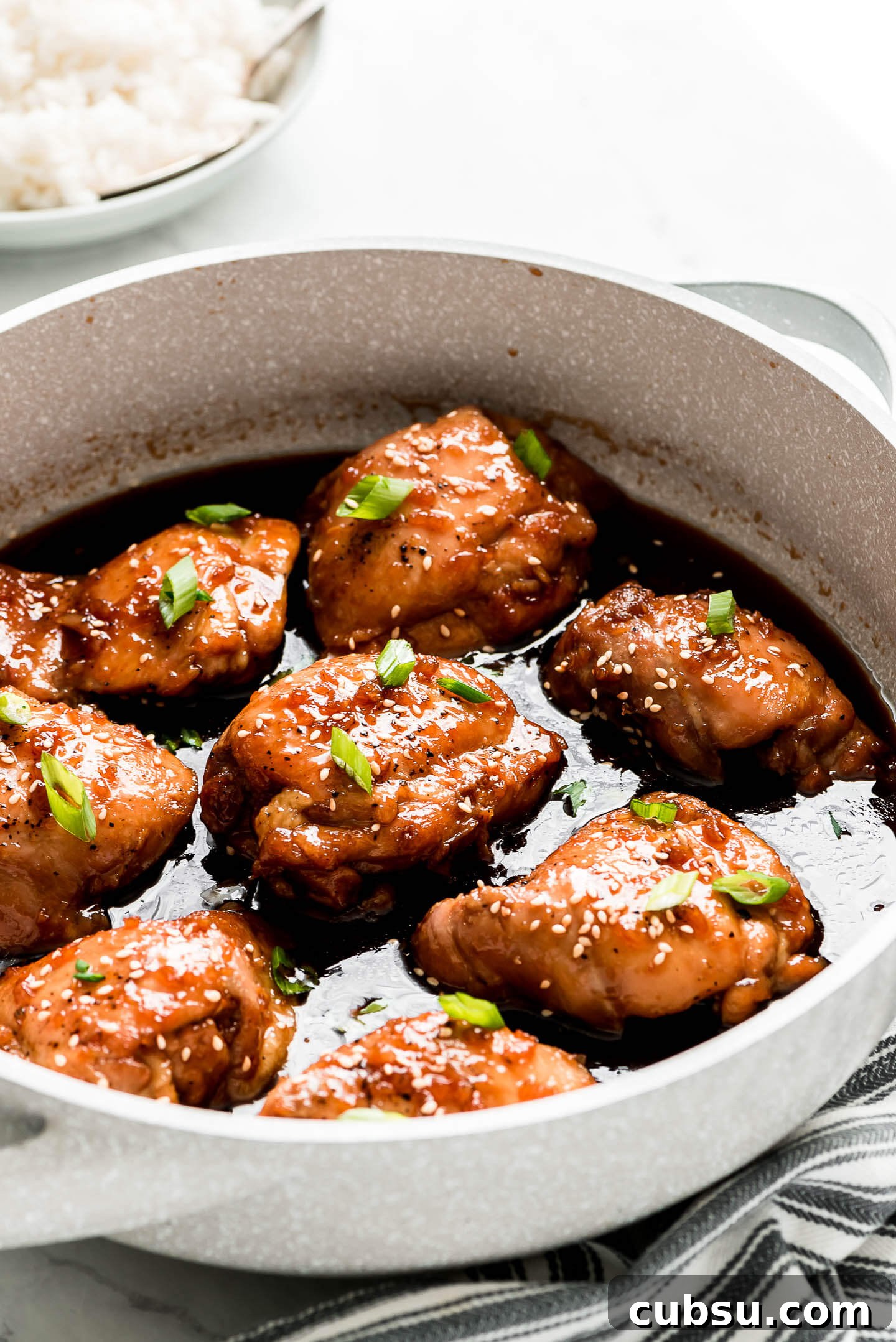Sticky Teriyaki Glazed Chicken Thighs with Garlic and Sesame 4 Teriyaki Chicken Thighs in a pan with sauce and garnished with sesame seeds and green onions.