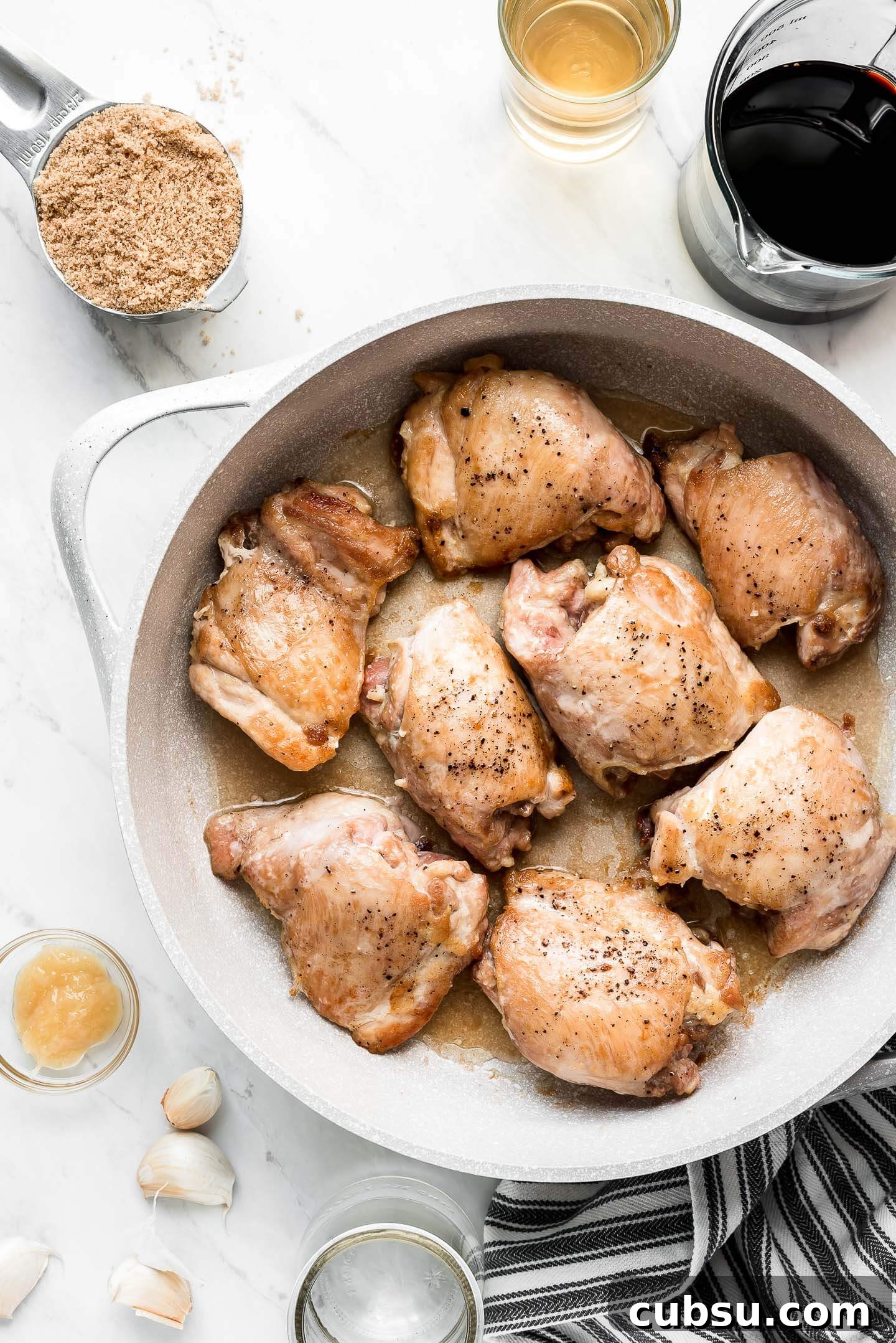 Sticky Teriyaki Glazed Chicken Thighs with Garlic and Sesame 5 Browned chicken thighs in a skillet seasoned with salt and pepper with various ingredients (brown sugar, soy sauce, vinegar, garlic, and ginger) surrounding.
