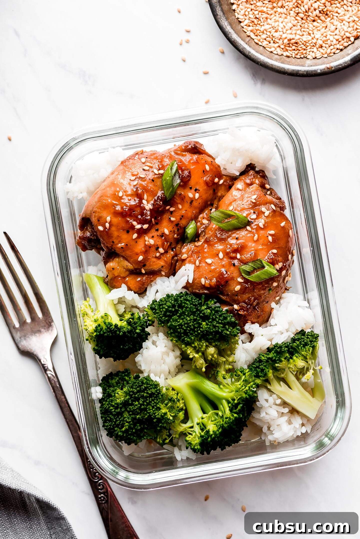 Sticky Teriyaki Glazed Chicken Thighs with Garlic and Sesame 7 A rectangle meal prep container with teriyaki chicken white rice, and broccoli.