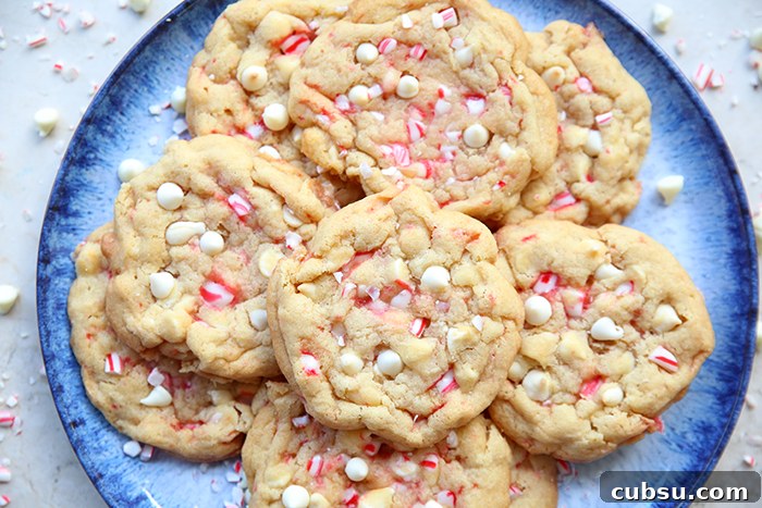 A large blue plate with a dark blue border filled with white chocolate peppermint cookies with white chocolate chips and peppermint pieces surrounding the plate.