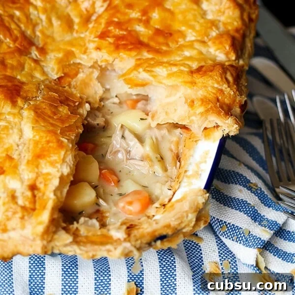 A dish of creamy chicken pie with puff pastry sat on a blue and white striped cloth.