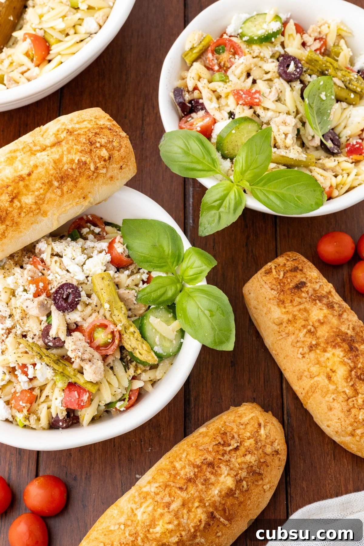 Mediterranean Tuna Orzo Salad with Olives, Feta & Lemon 12 Bowls of Mediterranean tuna orzo salad with vegetables, olives, and cheese, garnished with basil, on a wooden table. Two baguettes and cherry tomatoes are also visible.