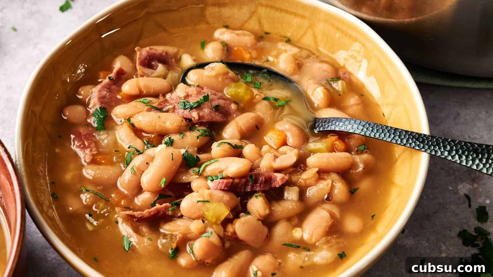 7 Holiday Ham Recipes to Make Dinner Feel Just Right 8 A bowl of white bean soup with pieces of ham, garnished with chopped parsley, and a spoon resting in the bowl.
