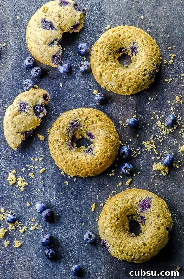Bird's eye view of three lemon blueberry cake donuts stacked on a black surface with some fresh blueberries scattered around