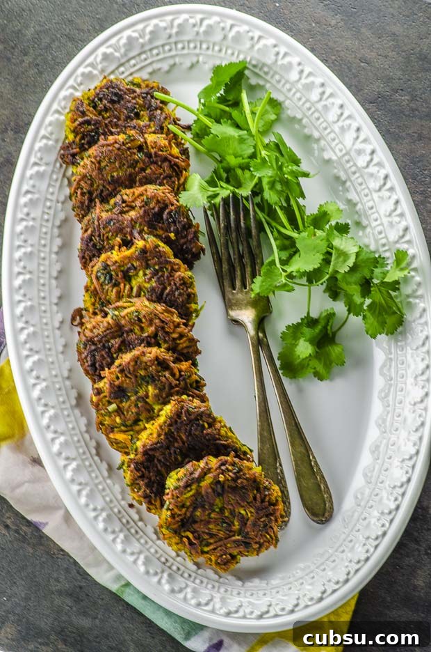 long oval plate with parsnip and carrot latkes on one side , two forks and a bunch of cilantro on the other side of the plate