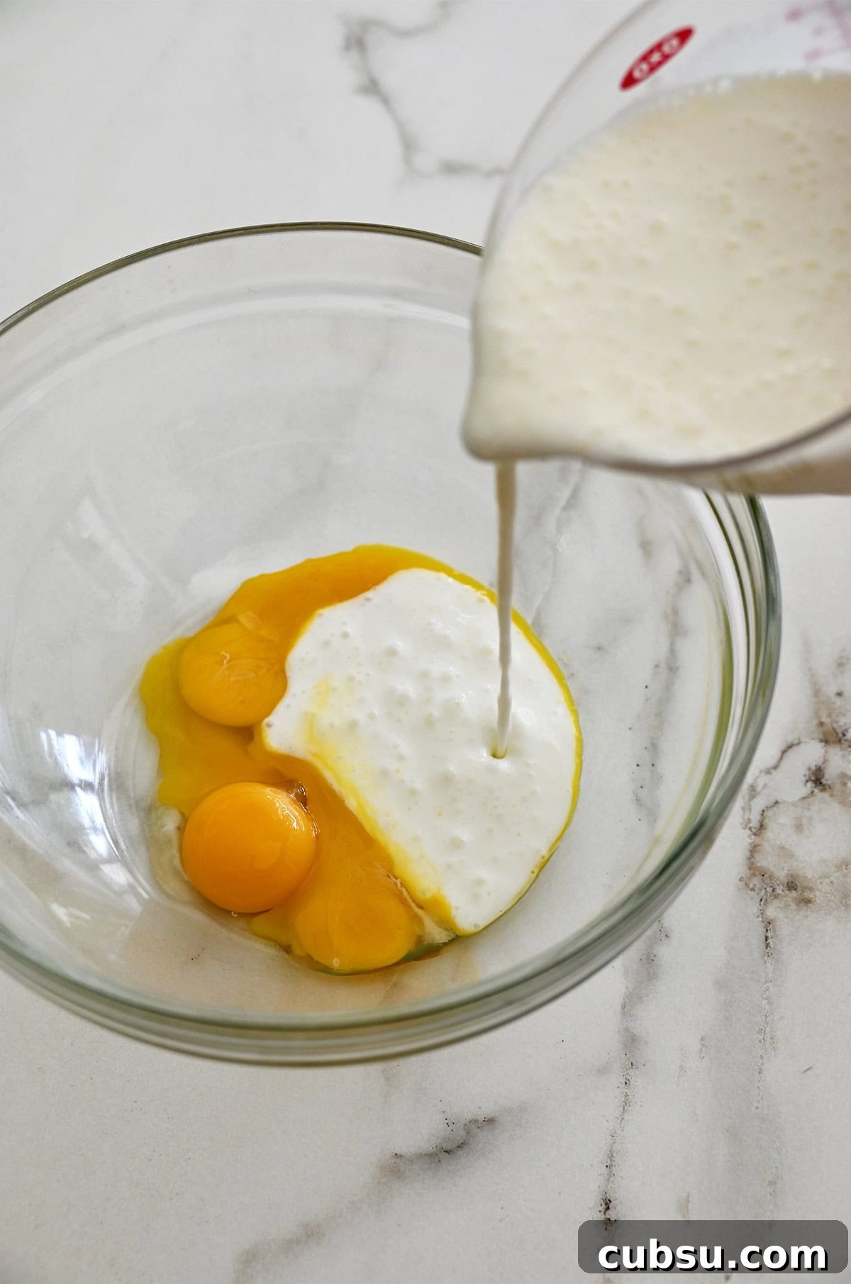 Crispy Belgian Waffles Recipe for Brunch and Weekend Mornings 4 Buttermilk being poured from a liquid measuring cup into a bowl with three egg yolks.