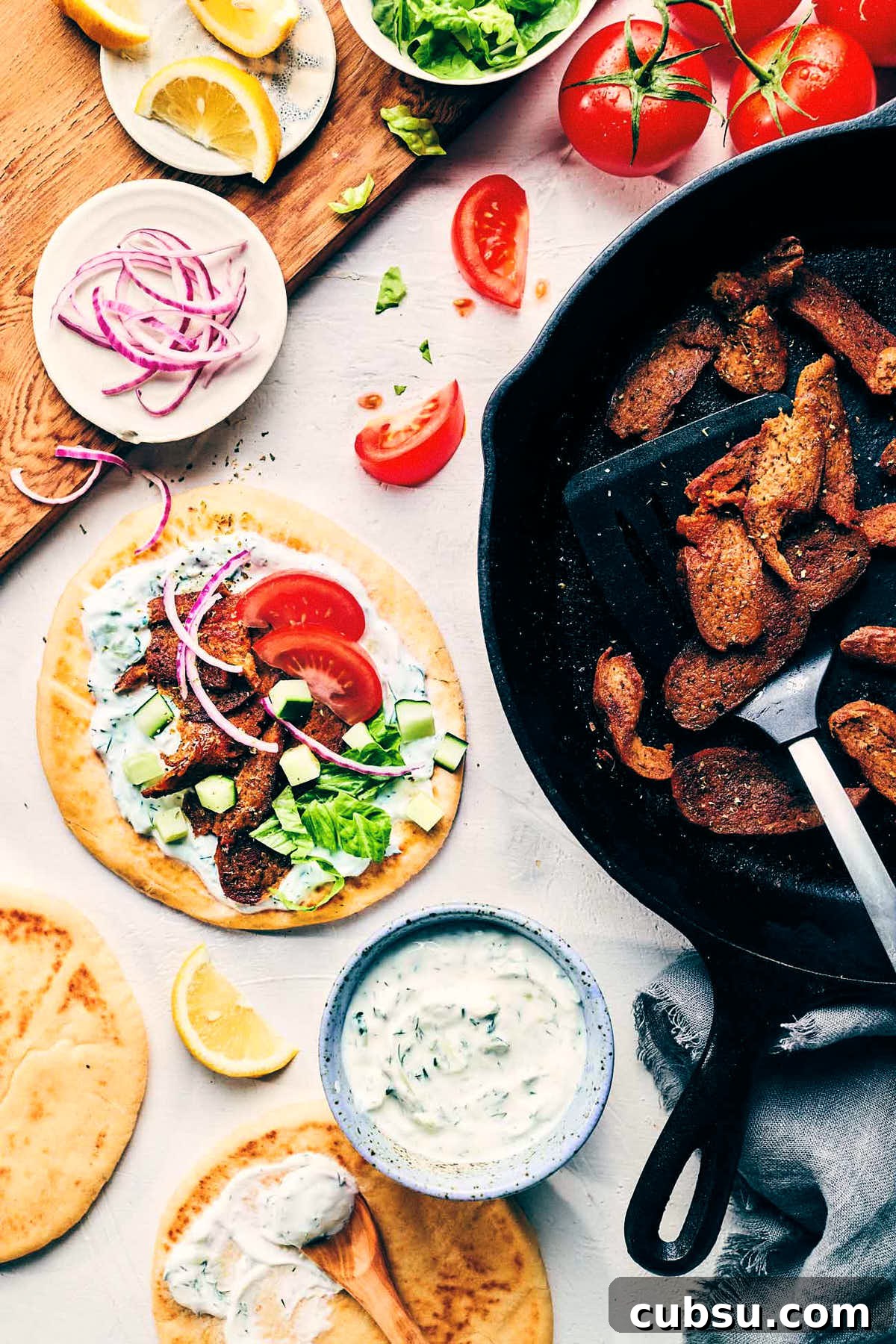 Seitan Vegan Gyros: Flavorful Plant-Based Greek Wrap Recipe 12 Table scene of greek gyros being topped with tomatoes and red onion