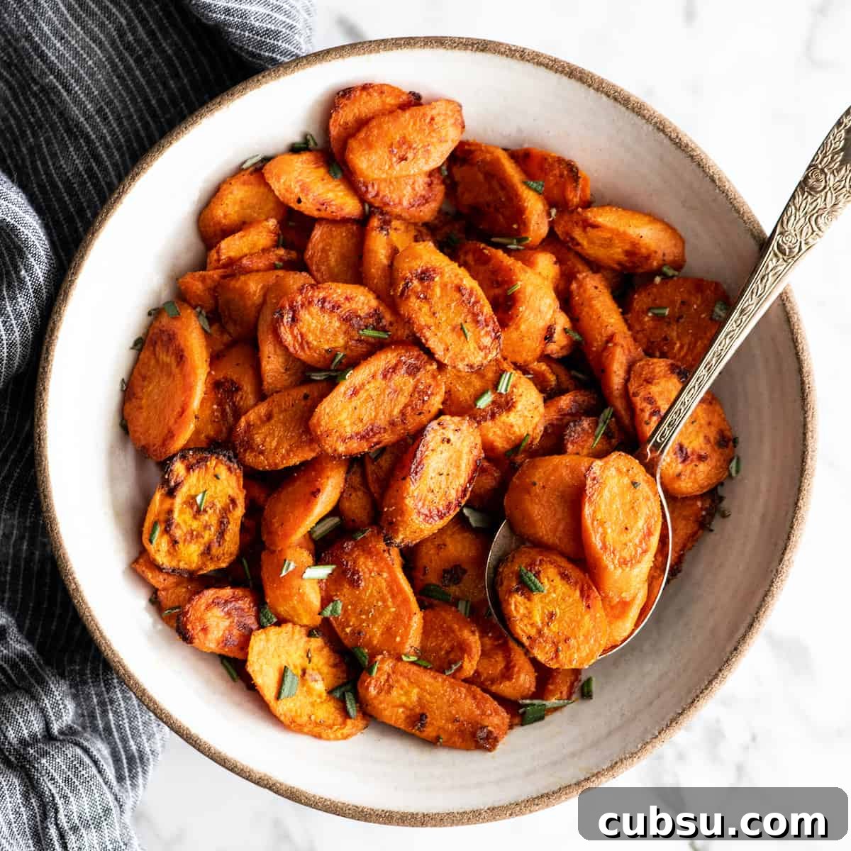 overhead view of roasted carrots in a bowl garnished with chopped rosemary with a spoon taking a portion out of the bowl