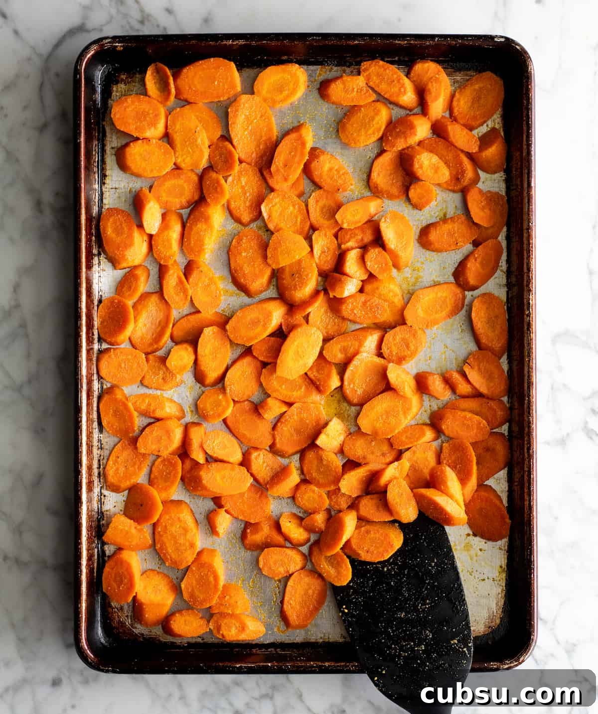overhead photo showing how to roast carrots - spatula stirring roasted carrots on a baking pan