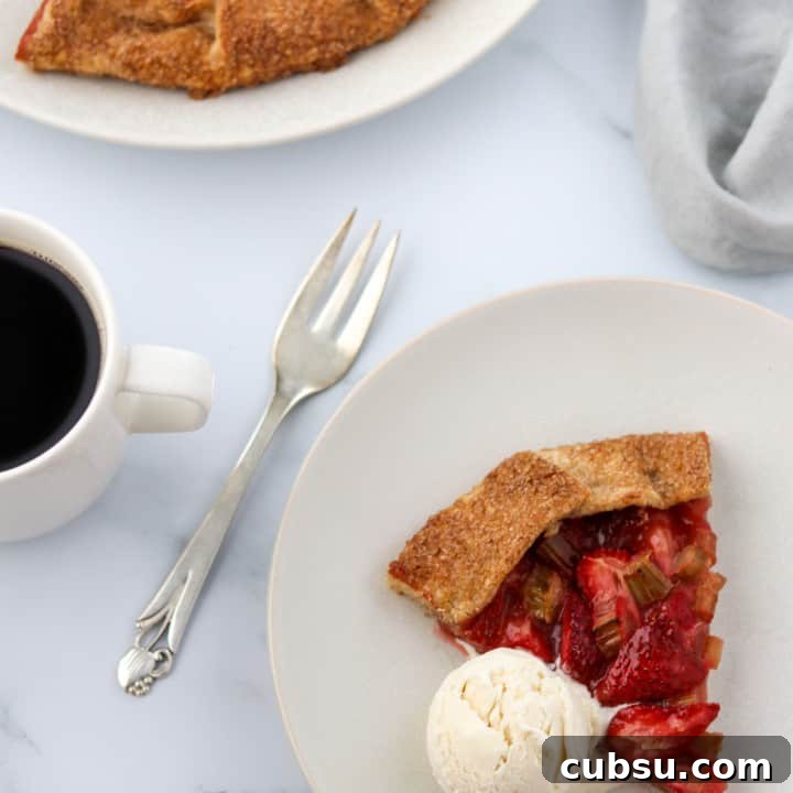 A slice of strawberry rhubarb galette with a scoop of ice cream and a fork and a cup of coffee